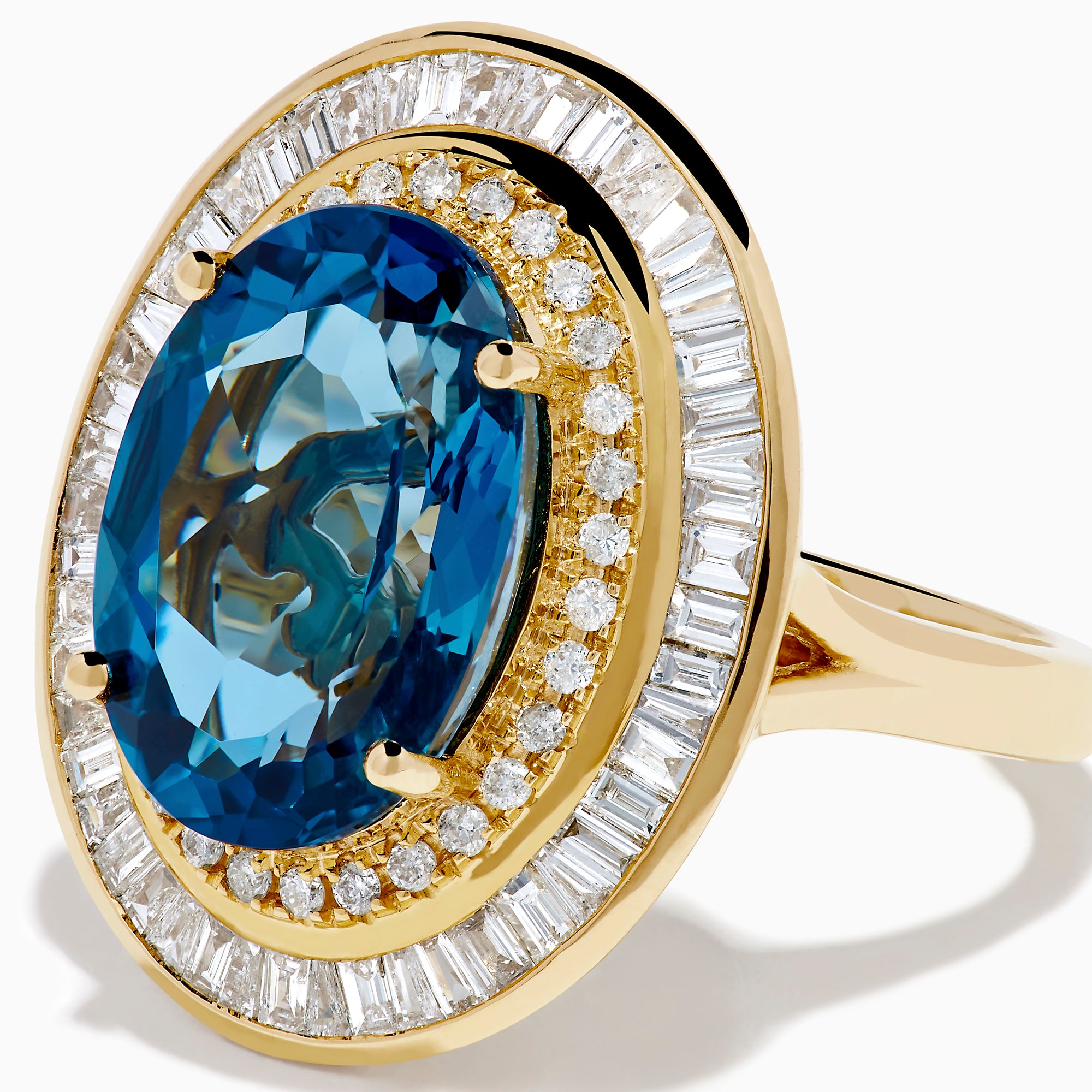 The 14K Yellow Gold London Blue Topaz and Diamond Double Halo Ring features an oval London Blue Topaz at the center, encircled by two halos of sparkling round and baguette-cut diamonds.