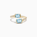 The Aquarius 14K Yellow Gold Aquamarine and Diamond Bypass Ring showcases two square-cut aquamarines facing each other, with sparkling round diamonds accenting one side of the band.