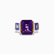 The 14K Yellow Gold Amethyst and Tanzanite 3 Stone Ring features a central emerald-cut amethyst with two rectangular tanzanites on each side, all set against a white background.