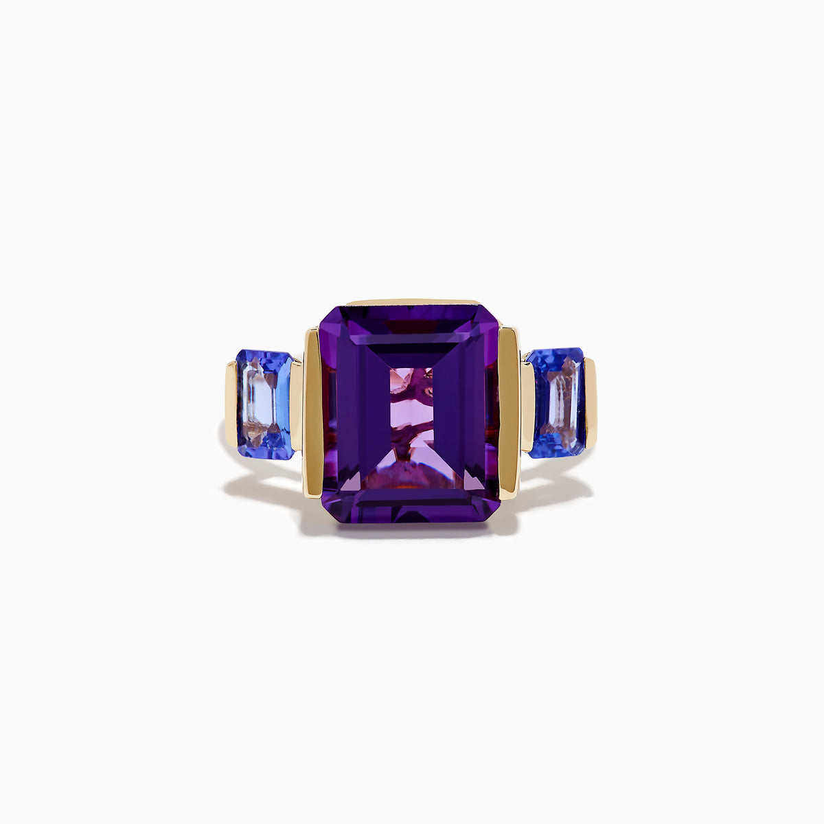 The 14K Yellow Gold Amethyst and Tanzanite 3 Stone Ring features a central emerald-cut amethyst with two rectangular tanzanites on each side, all set against a white background.