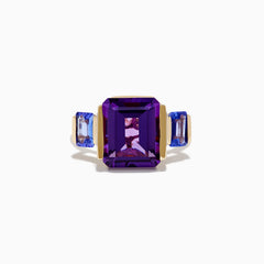 The 14K Yellow Gold Amethyst and Tanzanite 3 Stone Ring features a central emerald-cut amethyst with two rectangular tanzanites on each side, all set against a white background.