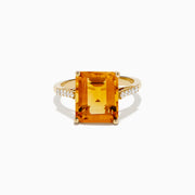The 14K Yellow Gold Step Cut Citrine and Diamond Cocktail Ring features a large rectangular citrine centerpiece with small round diamonds set along the band on each side of the main stone.