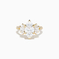 The Lab Grown Marquise Diamond 3 Stone Ring in 14K Yellow Gold features a central lab-grown marquise diamond, flanked by two pear-shaped diamonds with additional smaller stones adorning the band, shown on a white background.