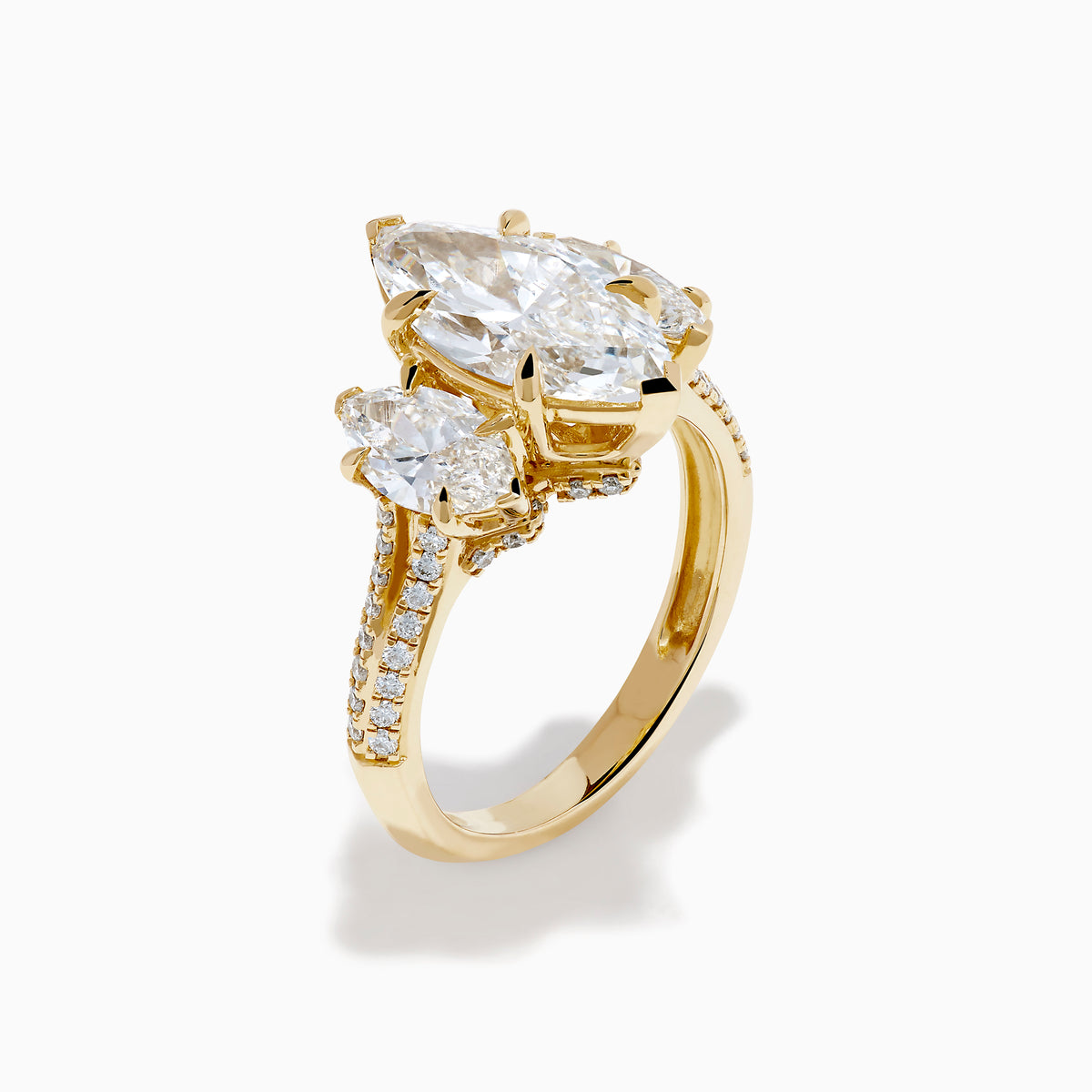 The Lab Grown Marquise Diamond 3 Stone Ring in 14K Yellow Gold features a central lab-grown marquise diamond, flanked by two pear-shaped diamonds with additional smaller stones adorning the band, shown on a white background.