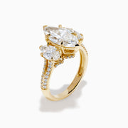 The Lab Grown Marquise Diamond 3 Stone Ring in 14K Yellow Gold features a central lab-grown marquise diamond, flanked by two pear-shaped diamonds with additional smaller stones adorning the band, shown on a white background.