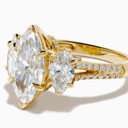 The Lab Grown Marquise Diamond 3 Stone Ring in 14K Yellow Gold features a central lab-grown marquise diamond, flanked by two pear-shaped diamonds with additional smaller stones adorning the band, shown on a white background.