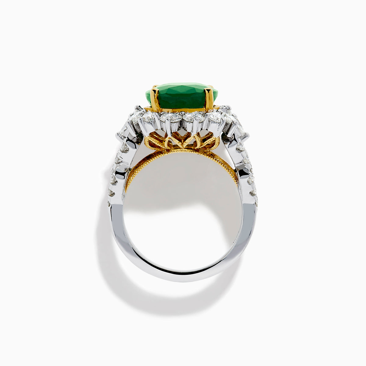 The 18K Two-Tone Gold Emerald, Yellow and White Diamond Ring features a striking oval green emerald surrounded by white diamonds, set in a gold and silver band with gold prongs, shown against a plain white background.