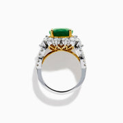 The 18K Two-Tone Gold Emerald, Yellow and White Diamond Ring features a striking oval green emerald surrounded by white diamonds, set in a gold and silver band with gold prongs, shown against a plain white background.