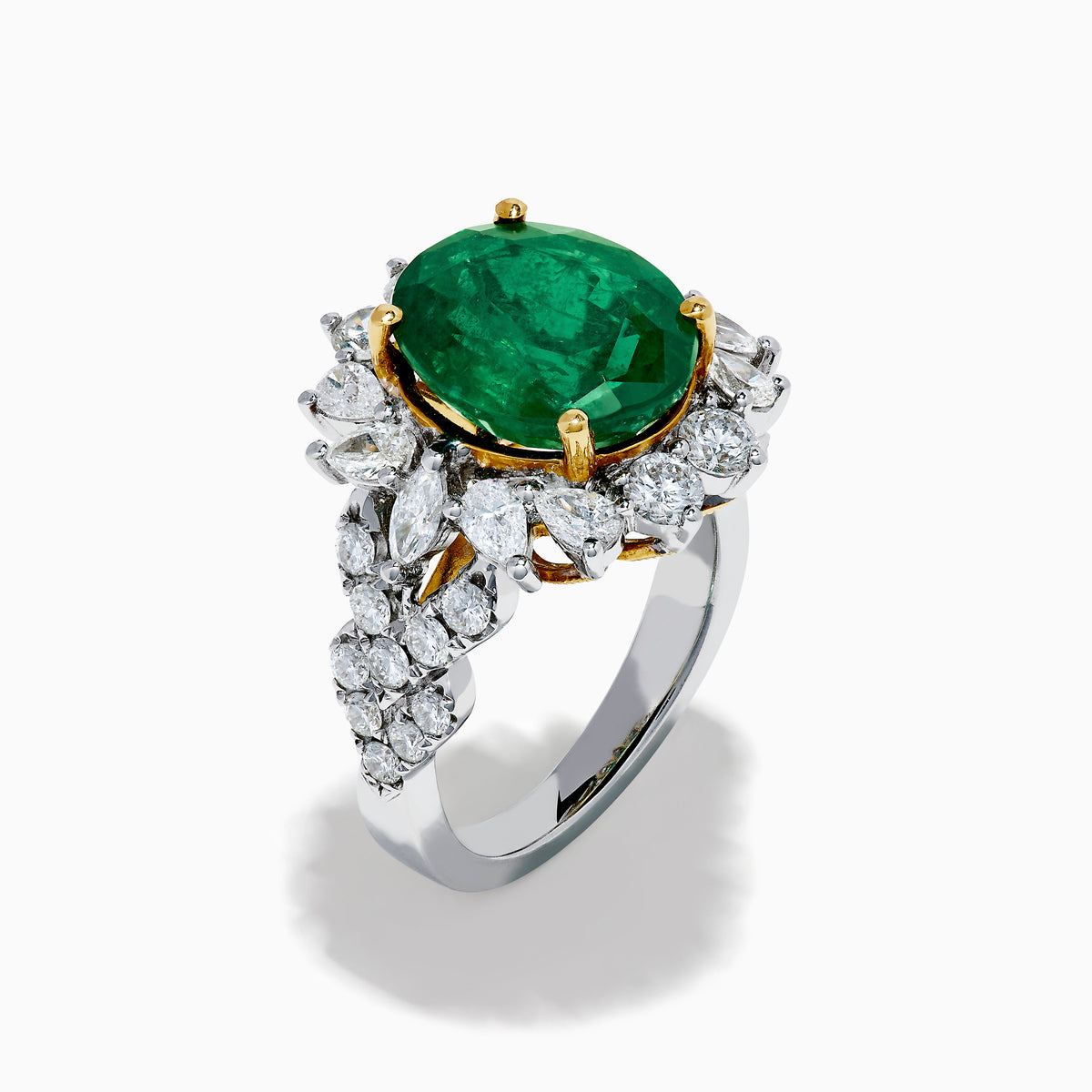 The 18K Two-Tone Gold Emerald, Yellow and White Diamond Ring features a striking oval green emerald surrounded by white diamonds, set in a gold and silver band with gold prongs, shown against a plain white background.