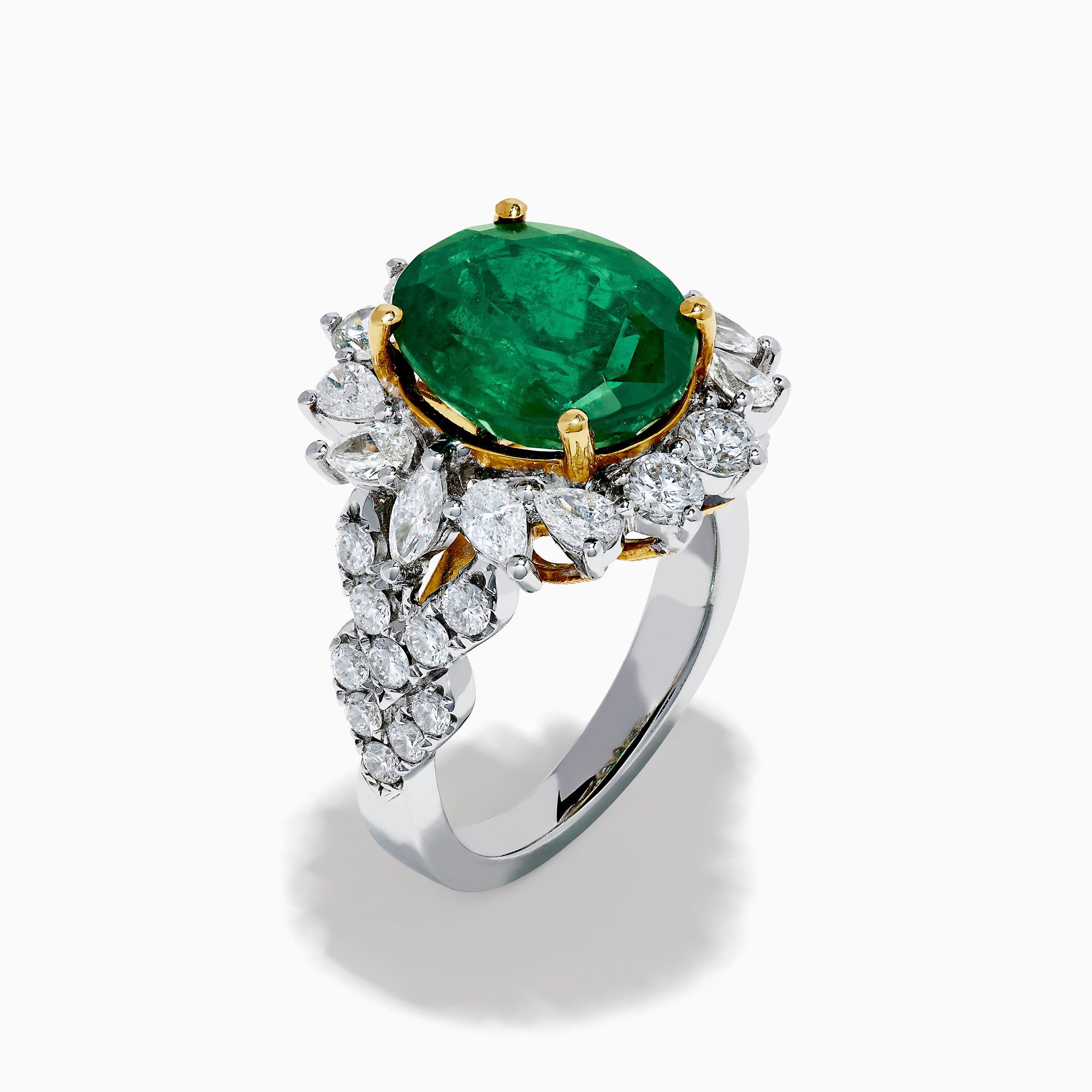 The 18K Two-Tone Gold Emerald, Yellow and White Diamond Ring features a striking oval green emerald surrounded by white diamonds, set in a gold and silver band with gold prongs, shown against a plain white background.