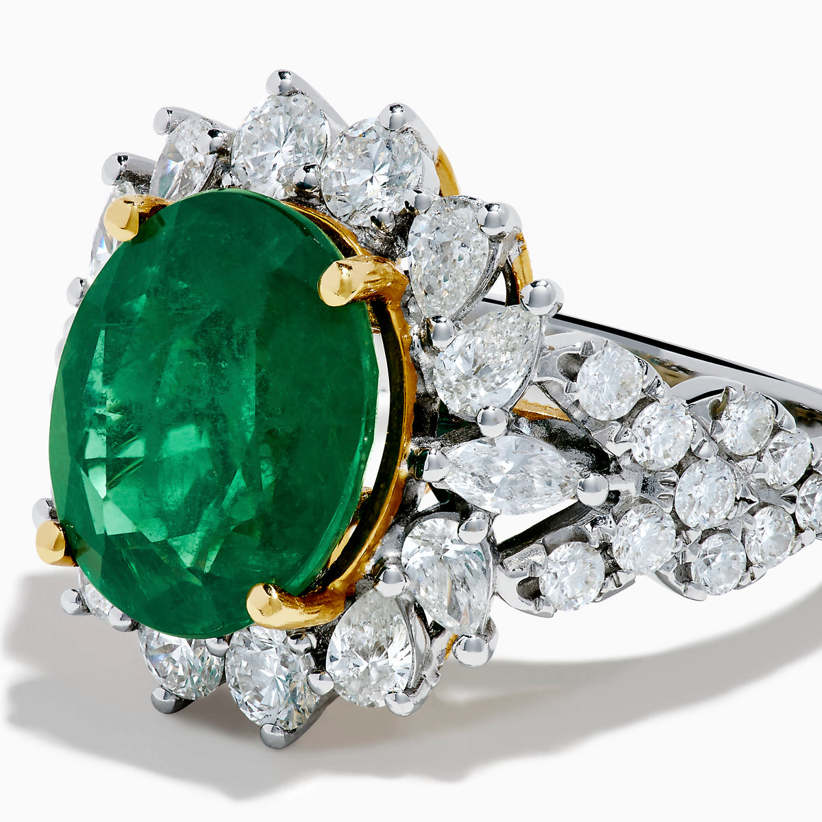 The 18K Two-Tone Gold Emerald, Yellow and White Diamond Ring features a striking oval green emerald surrounded by white diamonds, set in a gold and silver band with gold prongs, shown against a plain white background.