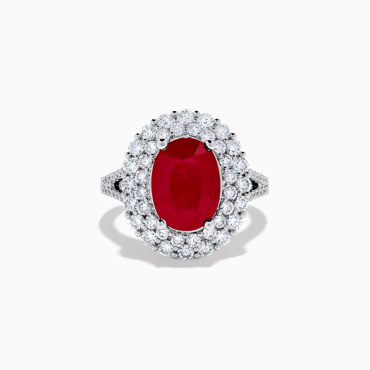The 18K White Gold Ruby and Diamond Double Halo Ring features an oval ruby encircled by double diamond halos on a sleek white gold band, showcased against a white background.