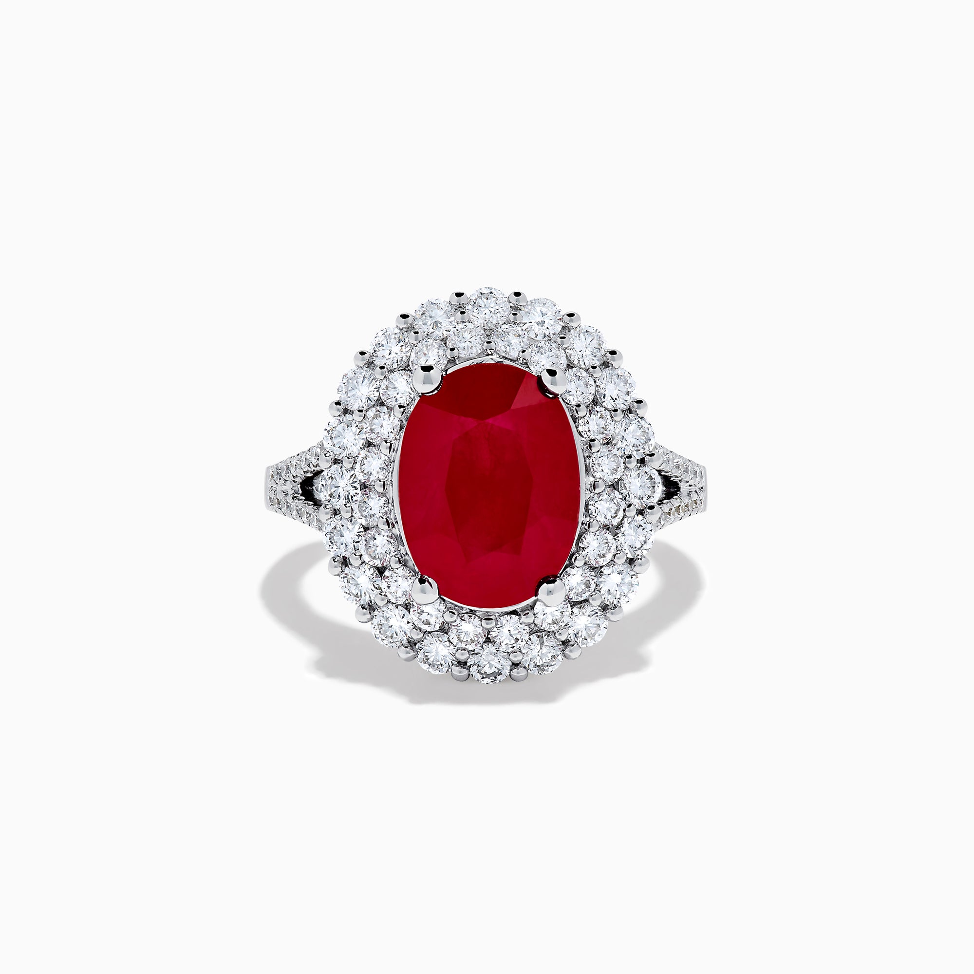 The 18K White Gold Ruby and Diamond Double Halo Ring features an oval ruby encircled by double diamond halos on a sleek white gold band, showcased against a white background.