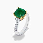 The 18K Two Tone Gold Emerald and Diamond Ring features a large square-cut green emerald in an 18K gold prong setting, with a white metal band accented by small round diamonds on each side.