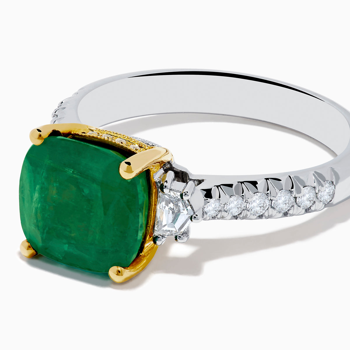 The 18K Two Tone Gold Emerald and Diamond Ring features a large square-cut green emerald in an 18K gold prong setting, with a white metal band accented by small round diamonds on each side.