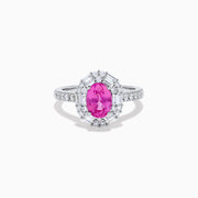 The 18K White Gold Pink Sapphire and Diamond Halo Ring showcases an oval pink sapphire center, encircled by a halo of baguette and round-cut diamonds, with more diamonds adorning the band.