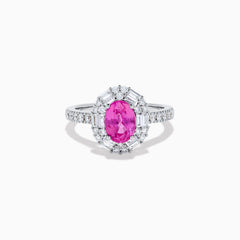 The 18K White Gold Pink Sapphire and Diamond Halo Ring showcases an oval pink sapphire center, encircled by a halo of baguette and round-cut diamonds, with more diamonds adorning the band.