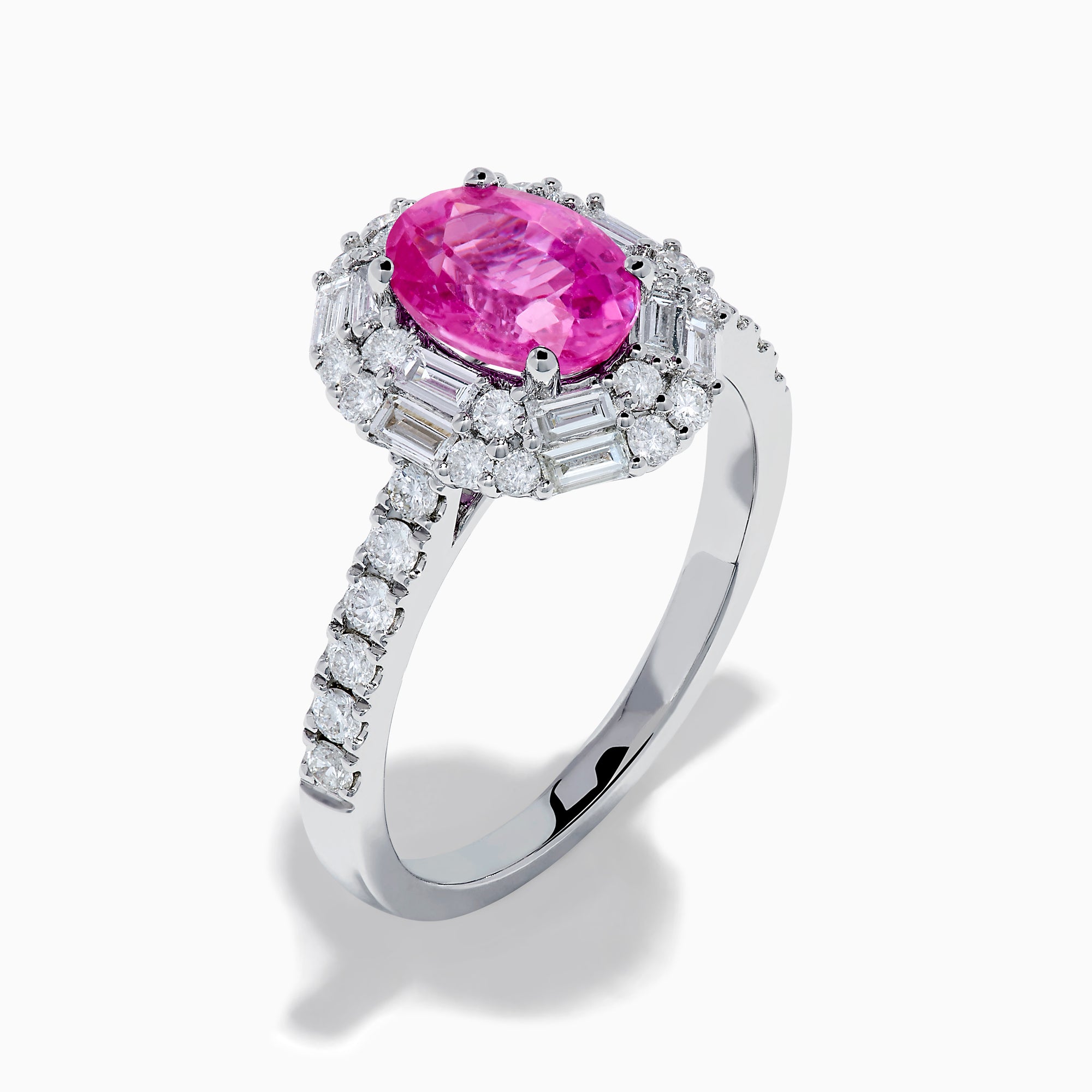 The 18K White Gold Pink Sapphire and Diamond Halo Ring showcases an oval pink sapphire center, encircled by a halo of baguette and round-cut diamonds, with more diamonds adorning the band.