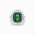 The 18K White Gold Green Sapphire and Diamond Halo Ring showcases a large oval green sapphire, surrounded by round and rectangular white diamonds, set on an elegant white gold band and displayed on a white background.
