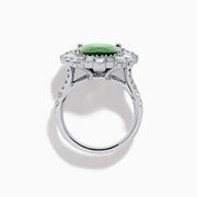 The 18K White Gold Green Sapphire and Diamond Halo Ring showcases a large oval green sapphire, surrounded by round and rectangular white diamonds, set on an elegant white gold band and displayed on a white background.