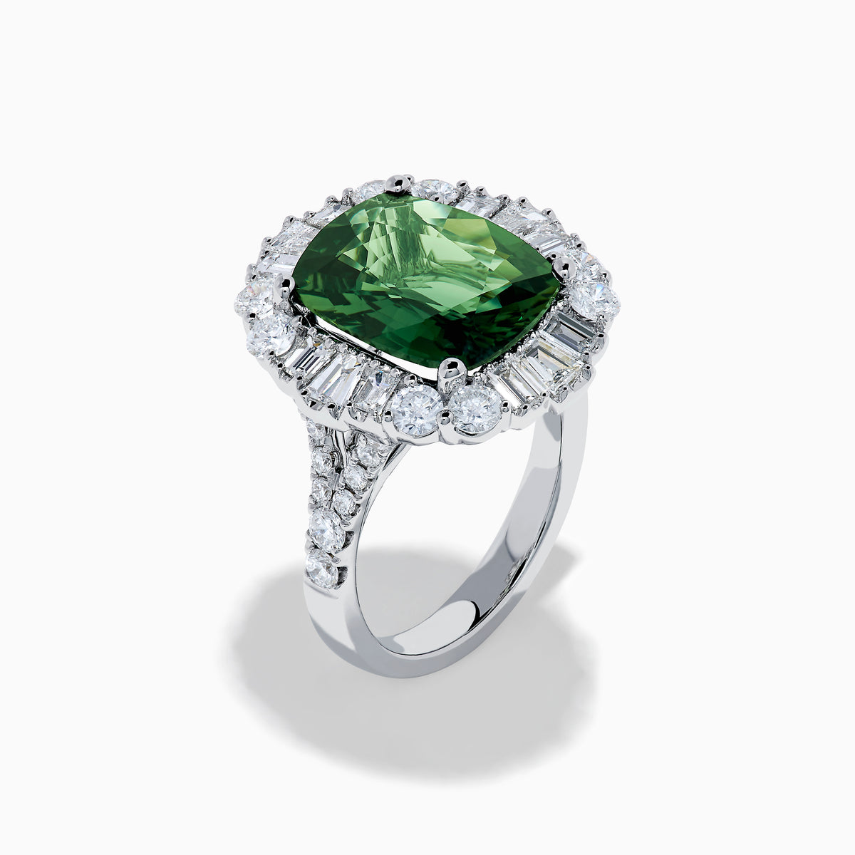 The 18K White Gold Green Sapphire and Diamond Halo Ring showcases a large oval green sapphire, surrounded by round and rectangular white diamonds, set on an elegant white gold band and displayed on a white background.
