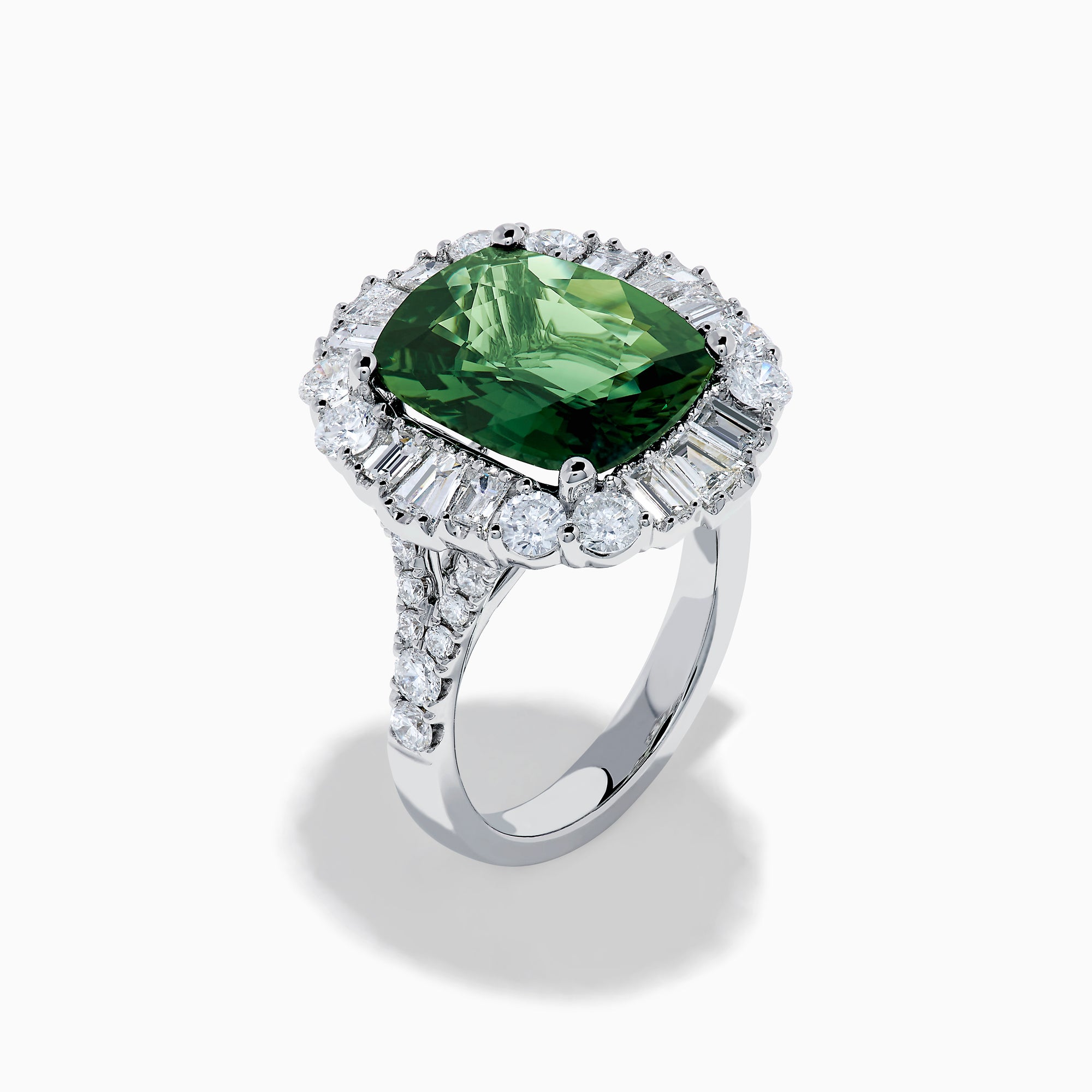 The 18K White Gold Green Sapphire and Diamond Halo Ring showcases a large oval green sapphire, surrounded by round and rectangular white diamonds, set on an elegant white gold band and displayed on a white background.