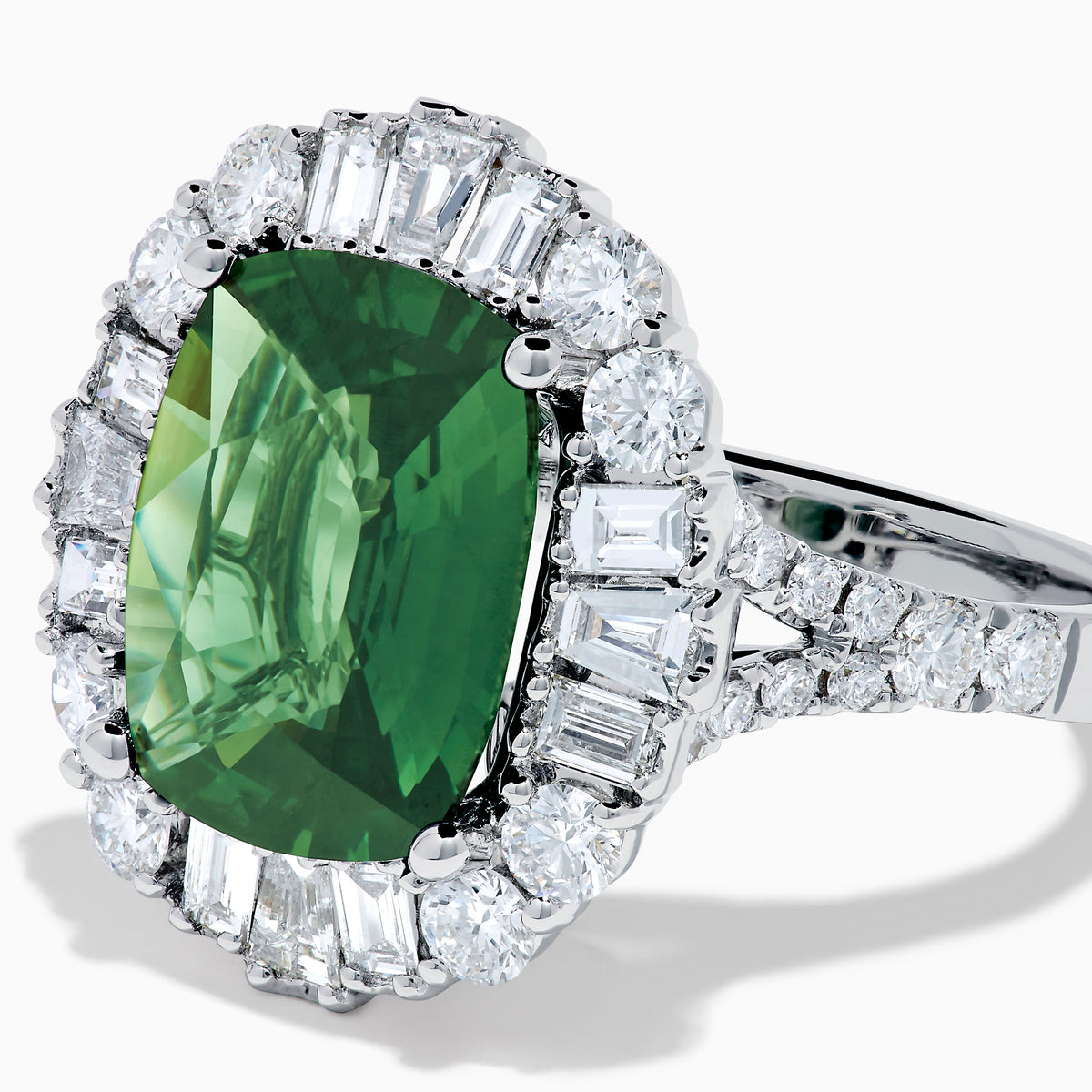 The 18K White Gold Green Sapphire and Diamond Halo Ring showcases a large oval green sapphire, surrounded by round and rectangular white diamonds, set on an elegant white gold band and displayed on a white background.