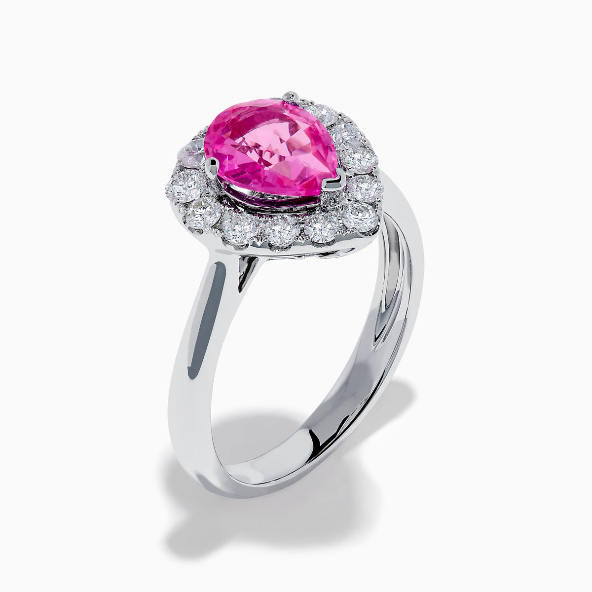 The 18K White Gold Pink Sapphire and Diamond Halo Ring features a pear-shaped pink sapphire center, accented by a sparkling diamond halo, elegantly displayed against a plain white background.