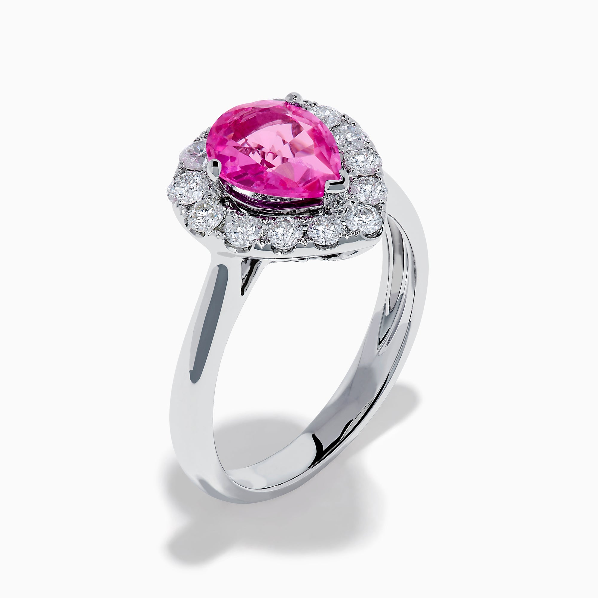 The 18K White Gold Pink Sapphire and Diamond Halo Ring features a pear-shaped pink sapphire center, accented by a sparkling diamond halo, elegantly displayed against a plain white background.