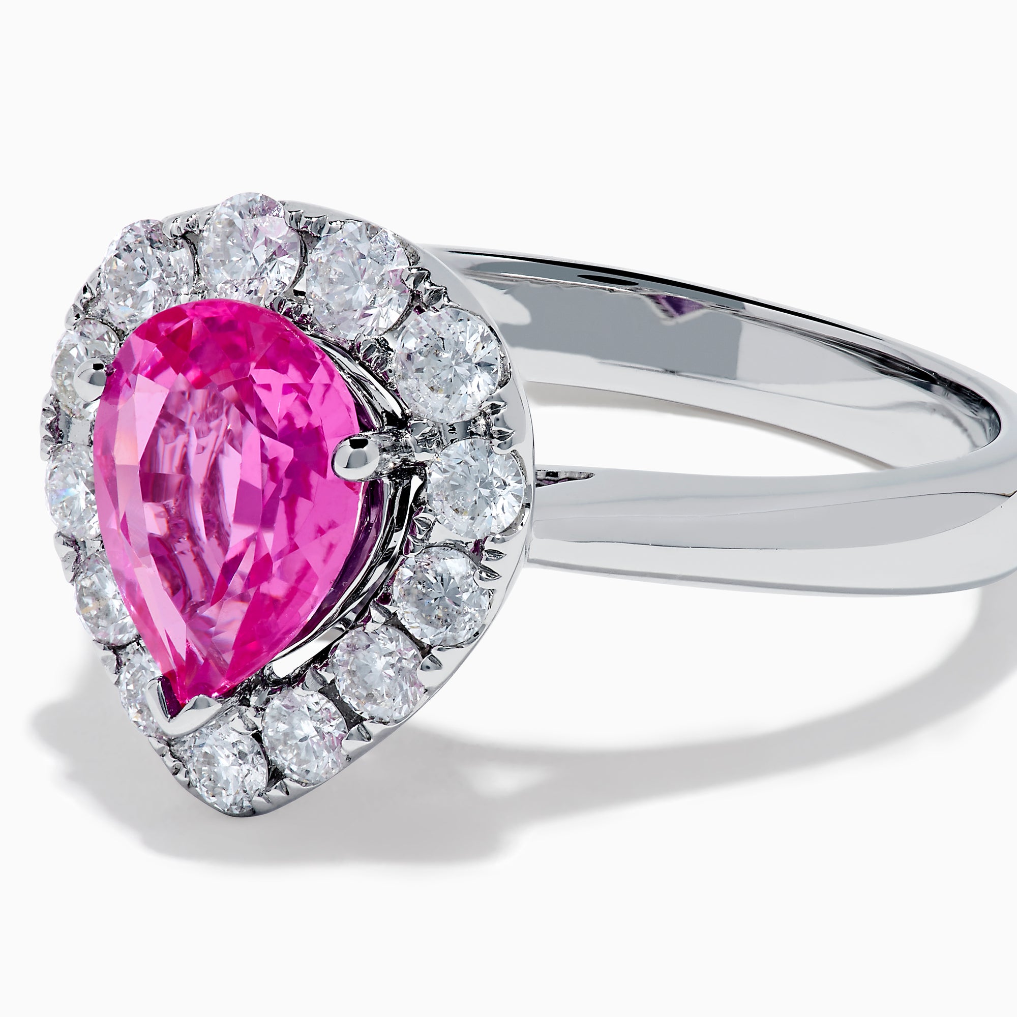 The 18K White Gold Pink Sapphire and Diamond Halo Ring features a pear-shaped pink sapphire center, accented by a sparkling diamond halo, elegantly displayed against a plain white background.