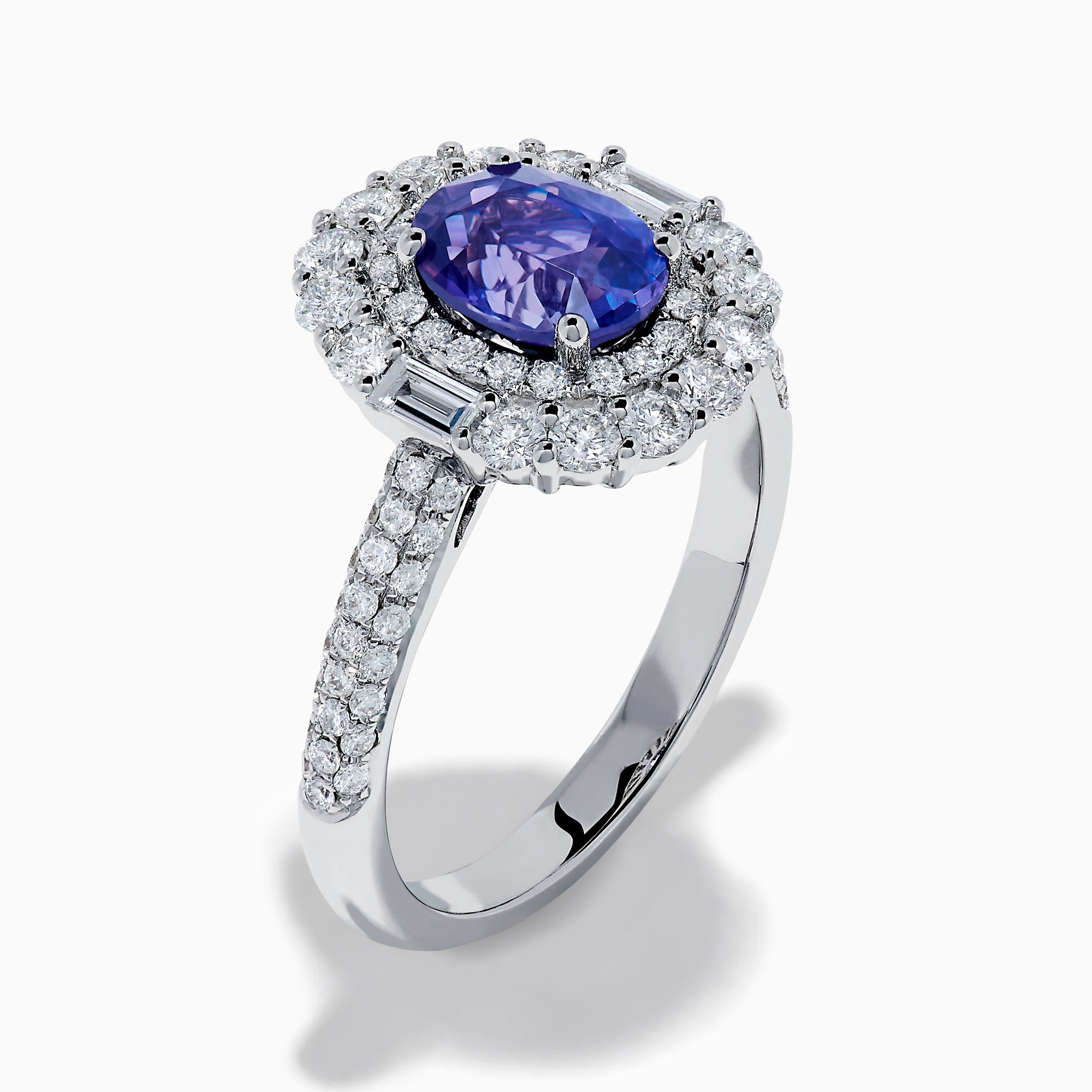 The 18K White Gold Purple Sapphire and Diamond Double Halo Ring features an oval purple sapphire center, two rows of white diamonds encircling it, and additional diamonds set along the band.