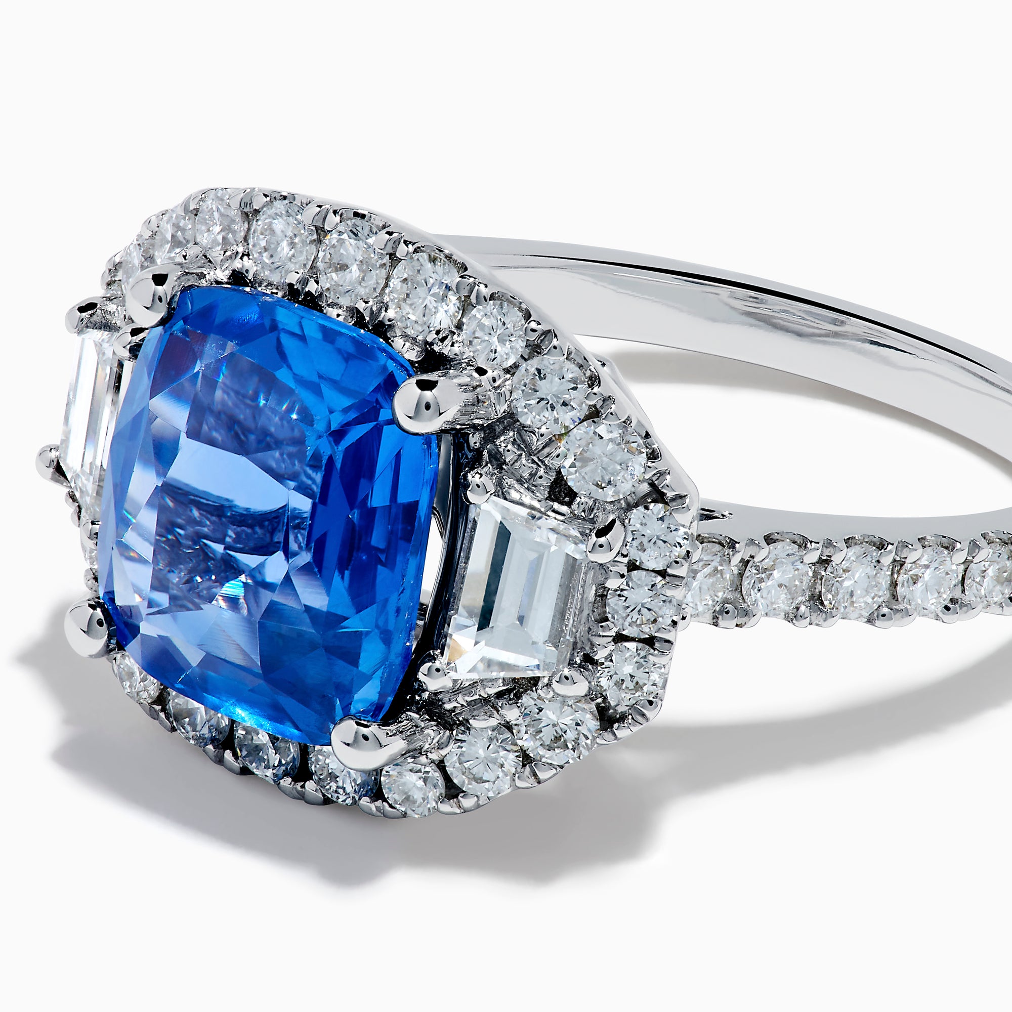 The Effy Hematian 18K Gold Cushion-Cut Blue Sapphire and Diamond Ring features a striking cushion-cut blue sapphire surrounded by a halo of round and baguette diamonds, all set in polished white 18K gold.