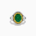 The 18K Gold Emerald, Yellow and White Diamond Double Halo Ring features a large oval green emerald center, surrounded by double halos of yellow and white diamonds with side diamonds on an 18K gold band. Set against a plain white background.