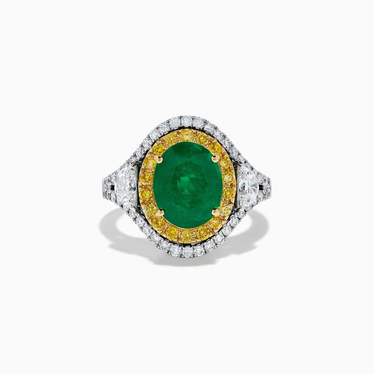The 18K Gold Emerald, Yellow and White Diamond Double Halo Ring features a large oval green emerald center, surrounded by double halos of yellow and white diamonds with side diamonds on an 18K gold band. Set against a plain white background.