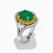 The 18K Gold Emerald, Yellow and White Diamond Double Halo Ring features a large oval green emerald center, surrounded by double halos of yellow and white diamonds with side diamonds on an 18K gold band. Set against a plain white background.