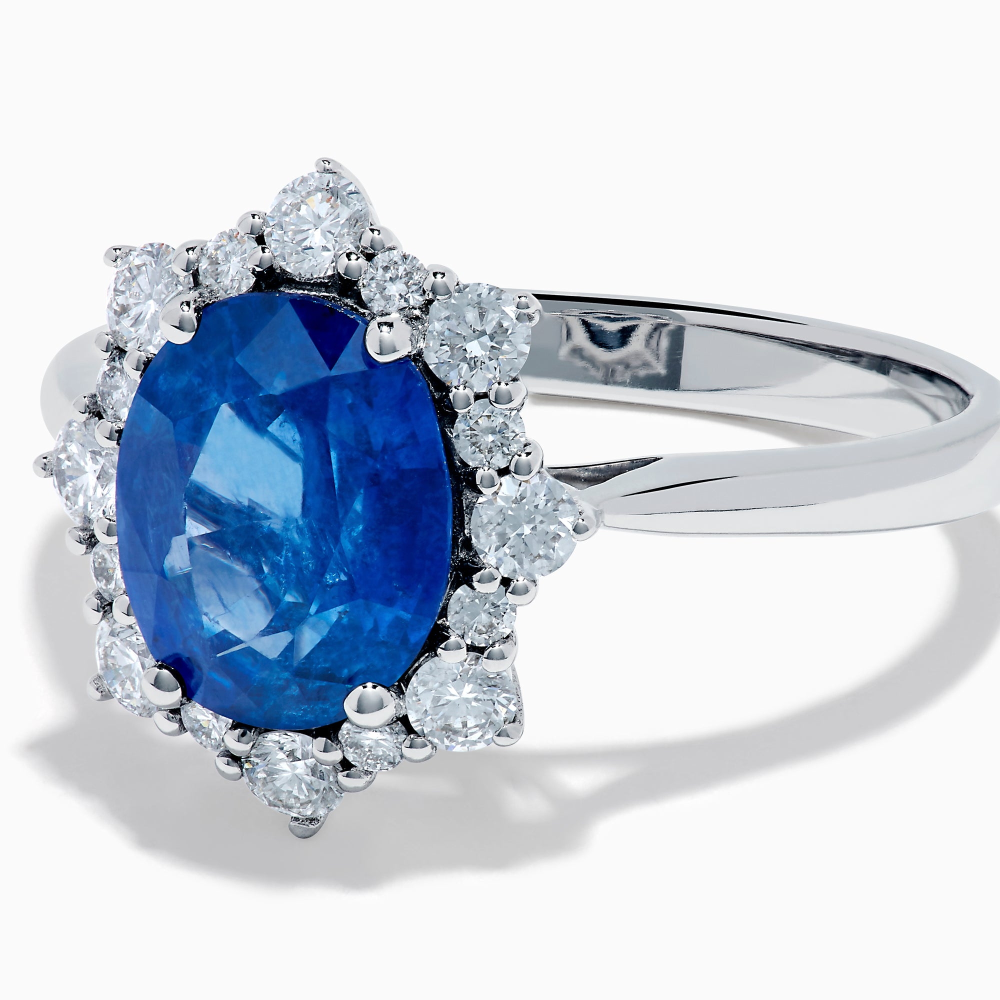 The Effy Hematian 14K White Gold Blue Sapphire and Diamond Halo Ring showcases an oval blue sapphire center, surrounded by a halo of sparkling round white diamonds, presented against a white background.