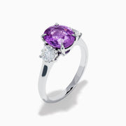 The Effy Hematian 18K White Gold Purple Sapphire and Diamond Three-Stone Ring features a large oval purple sapphire at the center with two smaller diamonds, shown on a white background.