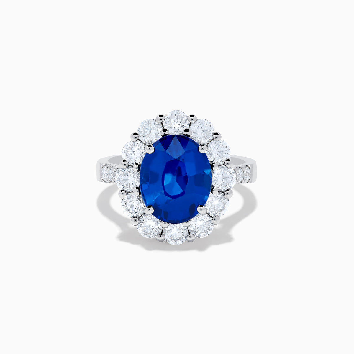 The 18K White Gold Blue Sapphire and Diamond Halo Ring features a large oval blue sapphire surrounded by a halo of round diamonds, showcased on a white background.