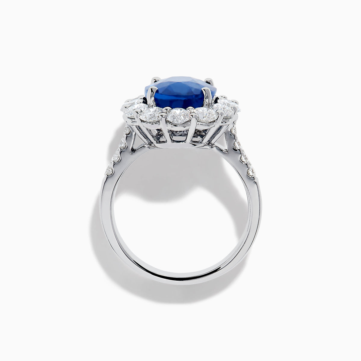 The 18K White Gold Blue Sapphire and Diamond Halo Ring features a large oval blue sapphire surrounded by a halo of round diamonds, showcased on a white background.