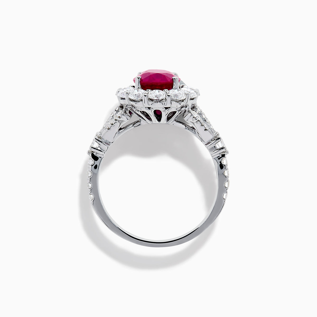 The 18K White Gold Ruby and Diamond Halo Ring features an oval red ruby at the center, encircled by a diamond halo, beautifully presented on a plain white background.