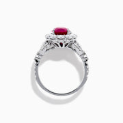 The 18K White Gold Ruby and Diamond Halo Ring features an oval red ruby at the center, encircled by a diamond halo, beautifully presented on a plain white background.