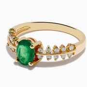 The 14K Yellow Gold Emerald and Diamond Ring showcases an oval green emerald center, framed by two rows of round diamonds on each side, set in yellow gold against a white background.