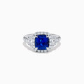 The Royale Bleu Platinum Blue Sapphire Halo Ring showcases a large cushion-cut sapphire surrounded by sparkling diamonds on a platinum band, set against a white background for a timeless, elegant look.