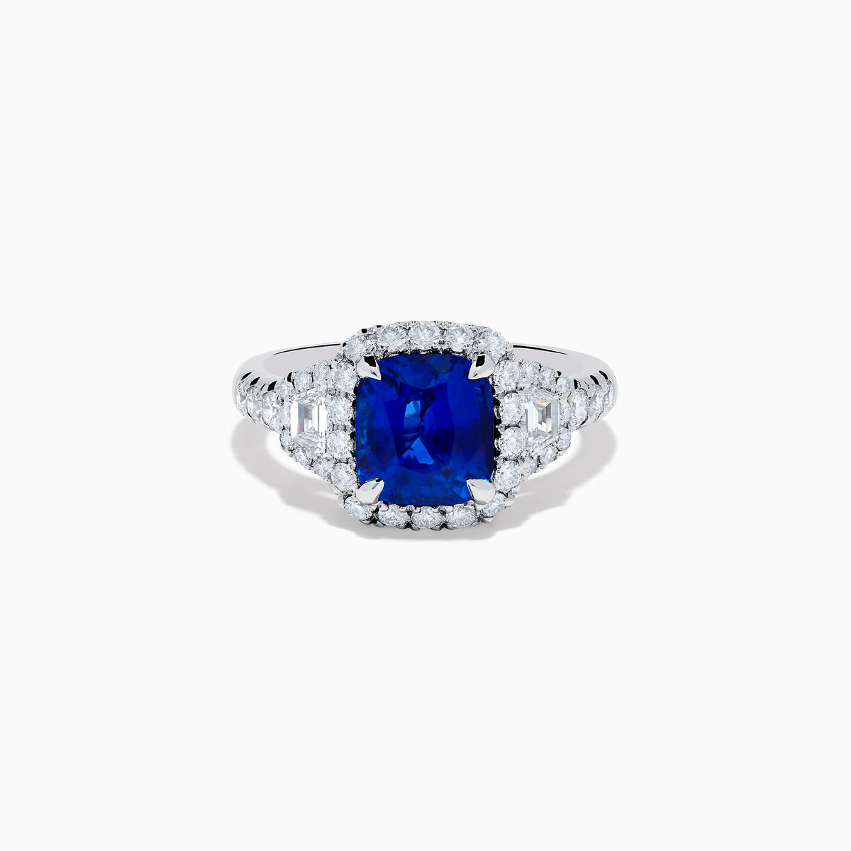 The Royale Bleu Platinum Blue Sapphire Halo Ring showcases a large cushion-cut sapphire surrounded by sparkling diamonds on a platinum band, set against a white background for a timeless, elegant look.