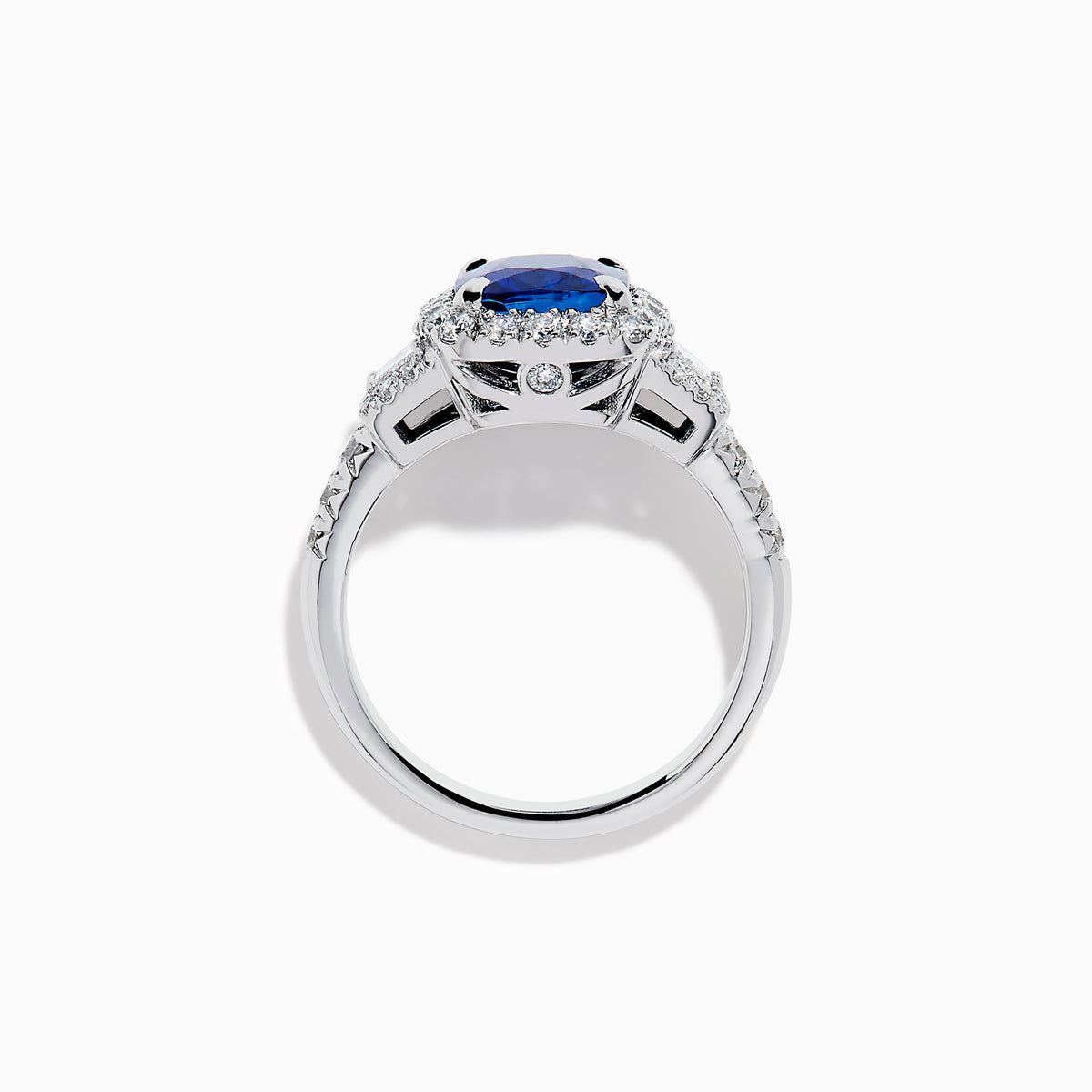 The Royale Bleu Platinum Blue Sapphire Halo Ring showcases a large cushion-cut sapphire surrounded by sparkling diamonds on a platinum band, set against a white background for a timeless, elegant look.