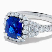 The Royale Bleu Platinum Blue Sapphire Halo Ring showcases a large cushion-cut sapphire surrounded by sparkling diamonds on a platinum band, set against a white background for a timeless, elegant look.