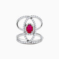 The Ruby Royale 14K White Gold Ruby and Diamond Ring features a central oval ruby with intersecting diamond-encrusted bands, beautifully set against a plain white background.