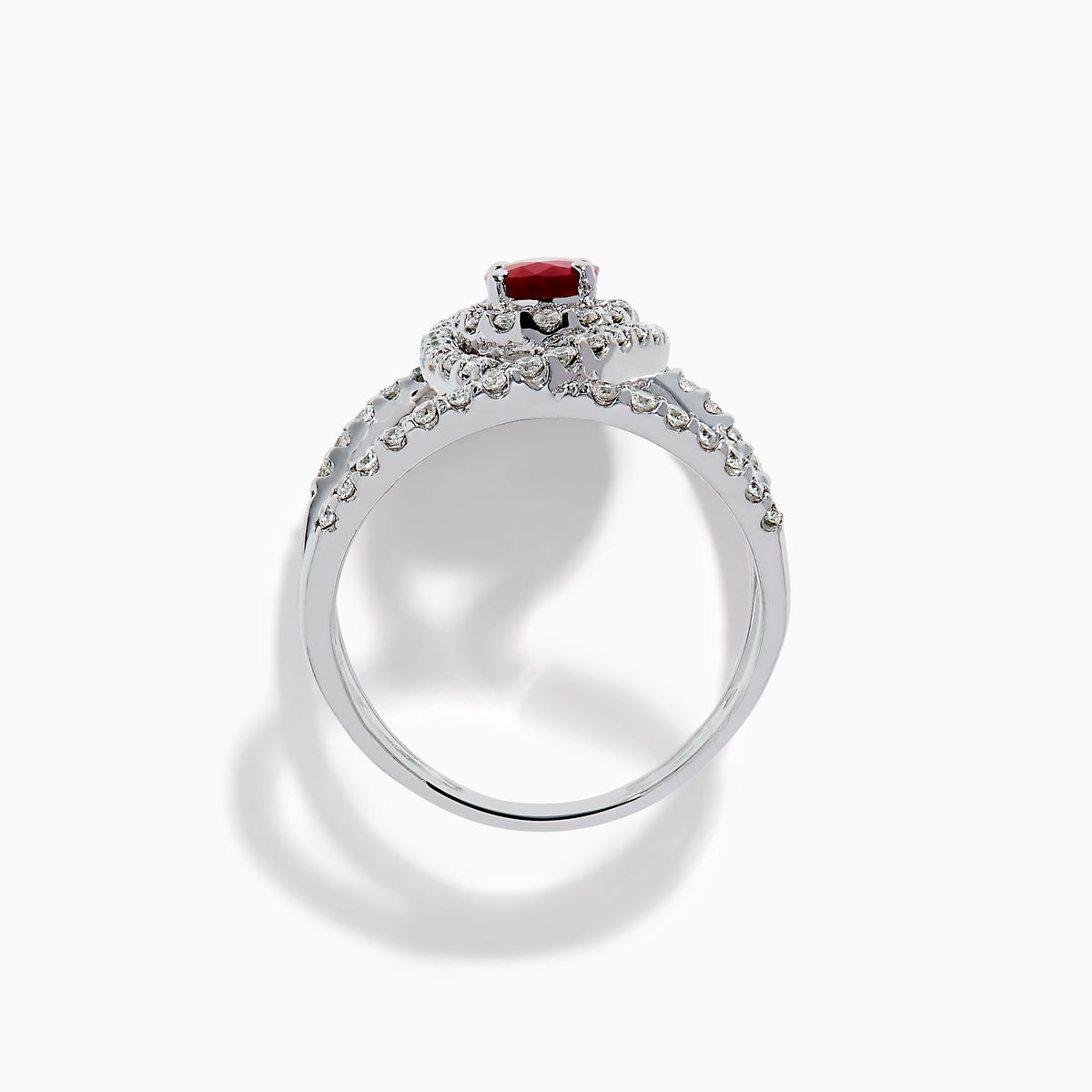 The Ruby Royale 14K White Gold Ruby and Diamond Ring features a central oval ruby with intersecting diamond-encrusted bands, beautifully set against a plain white background.