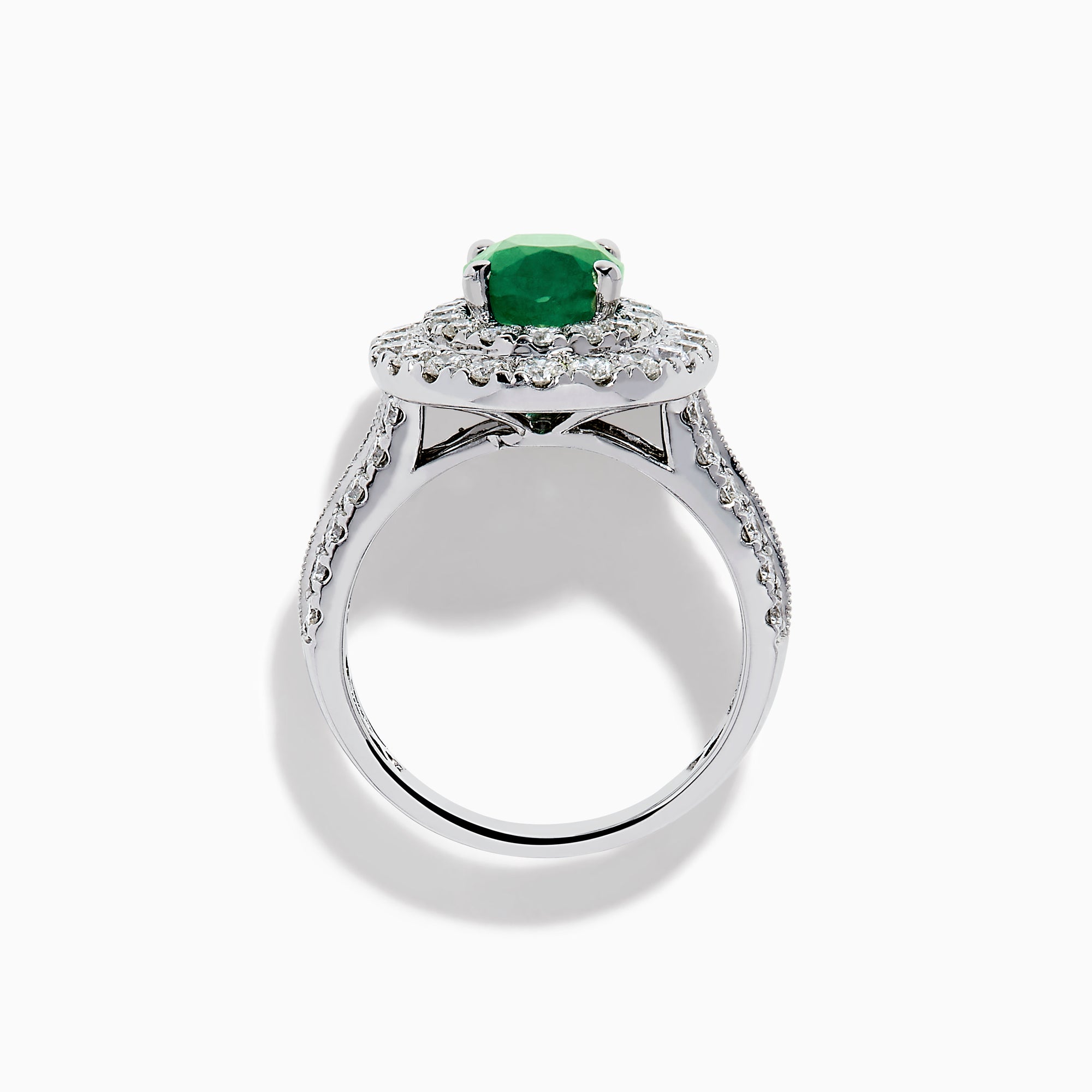 The Brasilica 18K White Gold Emerald and Diamond Double Halo Ring features an oval green emerald encircled by two rows of diamonds and delicate side stones, all set on a white gold band against a white background.