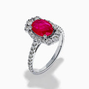 The Ruby Royale 14K White Gold Ruby and Diamond Ring showcases an oval red ruby center, a halo of round white diamonds, and additional diamonds along the band.